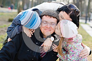 Happy family of 4 celebrating: Parents with two children having fun hugging & kissing father who is happy smile, closeup portrait