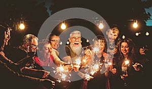 Happy family celebrating with sparklers fireworks at night party - Group of people with different ages and ethnicity having fun