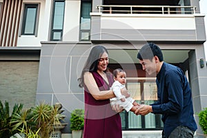 happy family, cheerful father and mother holding and playing with newborn baby while standing in front of their house