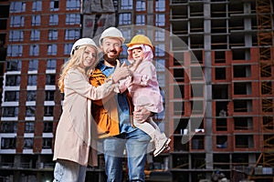 Happy family with child doing thumbs up sign at construction site.