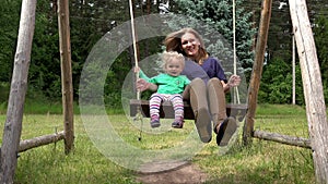 Happy family child girl and mother swinging on park playground.