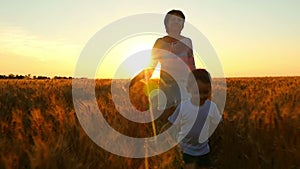 A happy family. The child and his mother are running across the field of golden wheat against the backdrop of the sunset