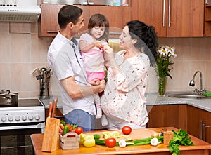 Happy family with child in home kitchen interior with fresh fruits and vegetables, pregnant woman, healthy food concept