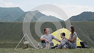 Happy family with a child laughing on campsite near a tent with a bonfire.