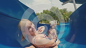 A happy family with a child is riding a water slide. Laughing, waving their hands at the camera