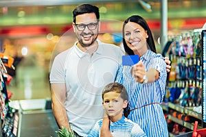Family with child and shopping cart buying food at grocery store or supermarket, woman holding credit card