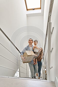 Happy family with child son carrying boxes going up stairs into new home.
