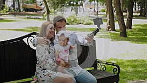 Happy family with a child take a selfie on a bench in the park.
