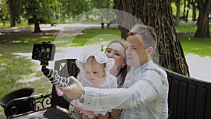 Happy family with a child take a selfie on a bench in the park.