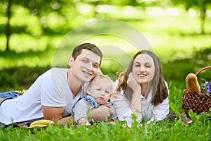 Happy family with a child during the weekend lie on their stomachs on the grass during a picnic in the park on a summer