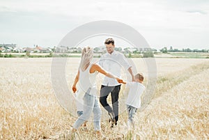 Happy family with children having fun round dancing holding hands together in wheat field