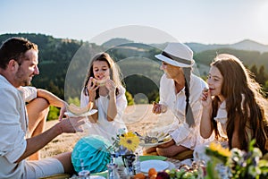 Happy family with children having picnic in park, parents with kids sitting eating healthy meals outdoors.