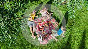 Happy family with children having picnic in park, parents with kids sitting on garden grass and eating healthy meals outdoors