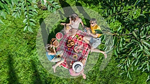 Happy family with children having picnic in park, parents with kids sitting on garden grass and eating healthy meals outdoors