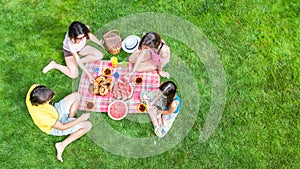 Happy family with children having picnic in park, parents with kids sitting on garden grass and eating healthy meals outdoors