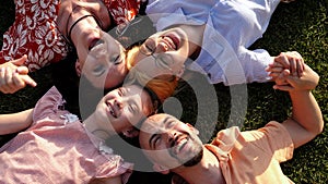 A happy family with children lying on the grass in a circle and laughing.