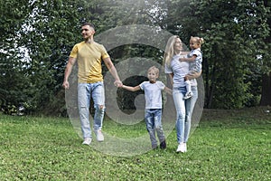 Happy family with children in the park on a sunny day. Mom, dad and little daughter and son in jeans and white t-shirts laugh and