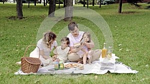 Happy family with children reading a book on a picnic outdoors.