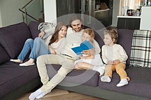 Happy family with children reading book together sitting on sofa