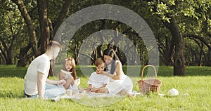 Happy family with children resting on the grass during a picnic in the picturesque green garden. Outdoors