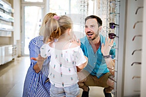 Happy family choosing glasses in optics store.