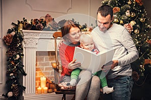 Happy family among Christmas decorations reading story in a book