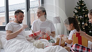 Happy family with Christmas gifts in bed at home