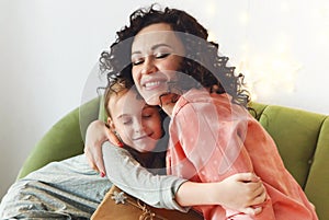 Happy family on Christmas morning, mother and daughter hugging while exchanging xmas gifts