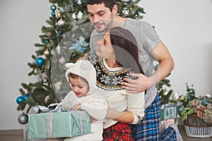 Happy family at christmas in morning opening gifts together near the fir tree. The concept of family happiness and well