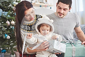 Happy family at christmas in morning opening gifts together near the fir tree. The concept of family happiness and well