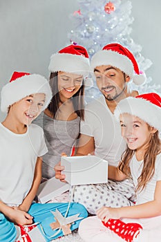 Happy family in Christmas morning opening present in home front of Christmas tree