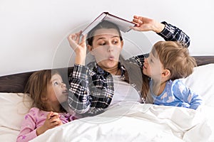 happy family. Close up loving mother lying with daughter son two kids pajamas in bed children reading interesting