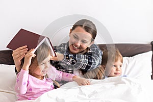 happy family. Close up loving mother lying with daughter son two kids pajamas in bed children reading interesting