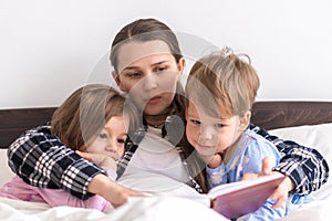 happy family. Close up loving mother lying with daughter son two kids pajamas in bed children reading interesting