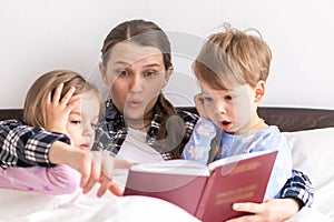 happy family. Close up loving mother lying with daughter son two kids pajamas in bed children reading interesting