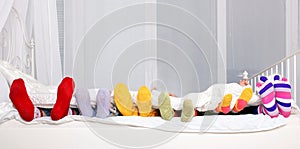 Happy family in colorful socks on white bed.