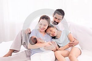 Happy family concept, father and daughter sit on bed excited looking new member in family, adorable newborn sleep on mother chest