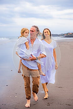 Happy family concept. Summer holidays. Family vacation in Asia. Mother, father and daughter walking barefoot along the beach.