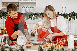 Happy family cooking Christmas cookies in the kitchen. Young smiling mother help her little son sprinkle flour on the dough.