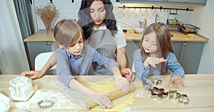 Happy family cooking dough for homemade cookies. Two cute children boy and girl helping mom in the kitchen