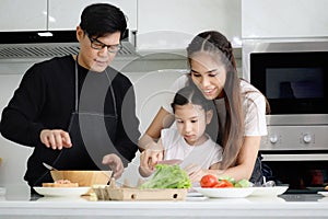 Happy family cooking at kitchen, father mother and cute daughter girl having fun during making meal at home. Parents and kid child