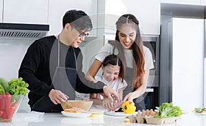 Happy family cooking together in the kitchen. Father, mother and cute little daughter turn vegetables to make salads