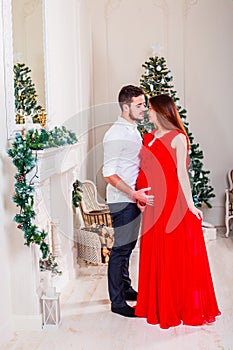Happy family couple on Christmas at fireplace. Happy couple kiss and hugging. Living room decorated by Xmas tree