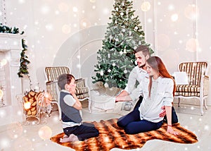 Happy family couple give gifts in the living room, behind the decorated Christmas tree, the light give a cozy atmosphere