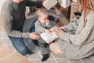 Happy family couple give gifts in the living room, behind the decorated xmas tree, the light give a cozy atmosphere. New Year