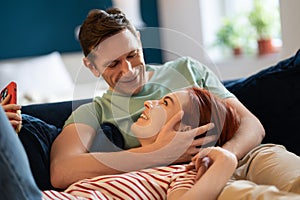 Happy family couple lovingly look at each other relaxing lying on sofa together sharing care at home