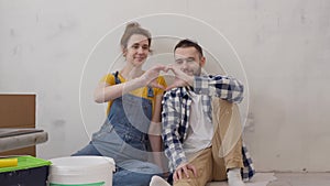 Happy family couple making hand heart looking on each other during apartment redecoration.