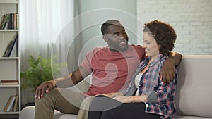 Happy family couple sitting on sofa talking and enjoying pastime with each other