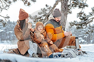 Happy family with cups of hot tea spending time together in winter forest