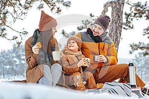 Happy family with cups of hot tea spending time together in winter forest